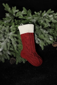 Detail of red cable knit Christmas stocking hanging on frosted pine branches with pine cones