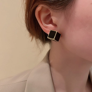 Gros plan d'une boucle d'oreille cubique noire minimaliste avec bordure dorée sur modèle