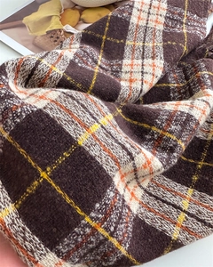Détail de la maille douce d'une écharpe à carreaux aux tons marron, blanc et orange chaud