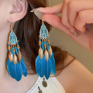 Bohemian dangle earrings with sky blue feathers and golden leaf charms worn by model