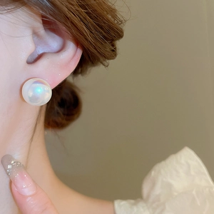Detailed close-up of a round mermaid pearl earring with radiant iridescent luster on ear