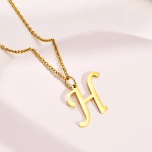 Detail showing high-polish gold H-letter pendant on a stainless steel chain