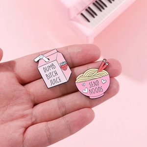 Detail of pink enamel pins featuring Dumb Bitch Juice and Send Noods humorous designs