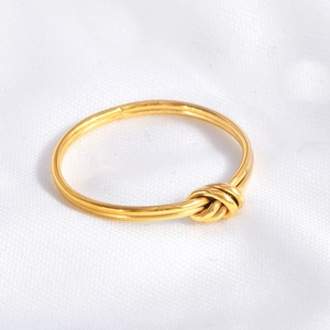 Detail of a minimalist gold knotted ring with a polished finish on white fabric