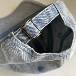 Close-up of light blue washed denim baseball cap with adjustable bronze metal buckle