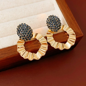 Detail of golden wavy hoop earrings featuring a deep blue crystal ball on a wooden tray