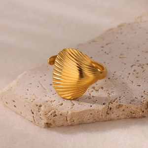 Detail view of a gold shell-shaped stainless steel ring on a textured beige stone base