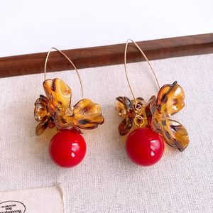 Détail de boucles d'oreilles fleurs en acrylique ambre avec perles rouges