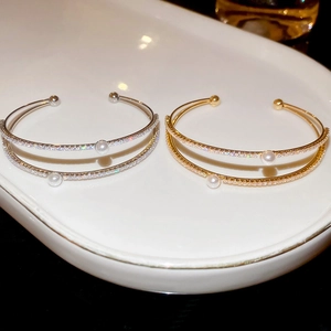 Detail of double-layer open bracelets with shiny zircons and white pearls in gold and silver