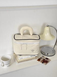 Detail of minimalist cream nylon makeup bag with crescent handle and contrast piping