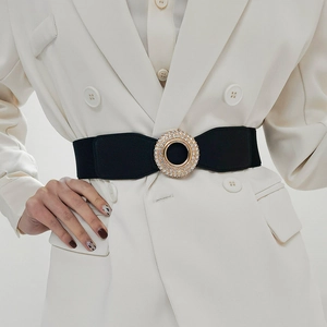 Detail of black elastic waist belt with large gold rhinestone buckle on white blazer