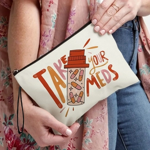 White canvas pouch with 'TAKE YOUR MEDS' print and wrist strap held by a person