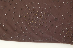 Dettaglio del tessuto a rete marrone con ricami di perline oro e argento sul top