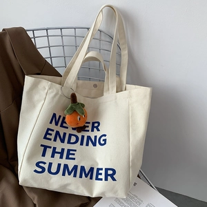 Close-up of beige canvas tote with blue summer slogan and persimmon charm pendant