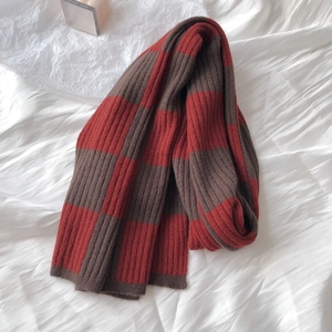 Detail of red and brown checkerboard knit scarf in thick wool blend on soft fabric