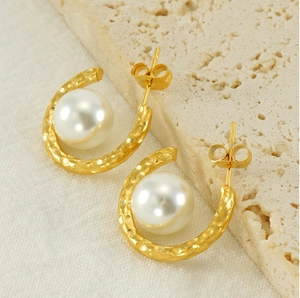 Détail de boucles d'oreilles dorées martelées en C avec de grandes perles blanches