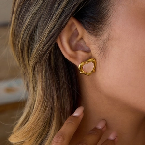 Pink heart-shaped earrings with gold wavy texture borders on a model ear