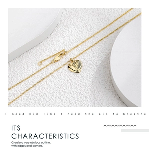Detail shot of a golden necklace with a unique heart and wing pendant on a white base