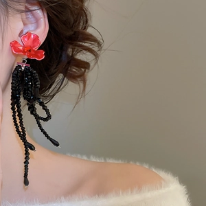 Détail de boucles d'oreilles fleur rouge avec de longs pompons noirs en perles