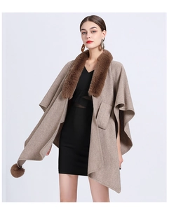 Detail of knitted poncho featuring brown faux rabbit fur collar and decorative pom-poms