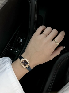 Elegant square women's watch with crystal-set bezel and black leather strap worn in a car