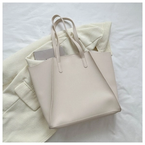 Close-up of beige PU leather tote bag on beige blazer and white sheets in minimalist style