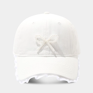 Detailed view of white baseball cap with pearl bow design and lace trim edges