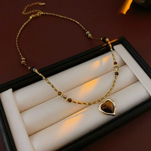 Détail du pendentif cœur ambré sur collier de perles dorées dans une boîte à bijoux chic