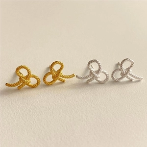Close-up of gold and silver knot earrings featuring detailed twisted rope metal texture