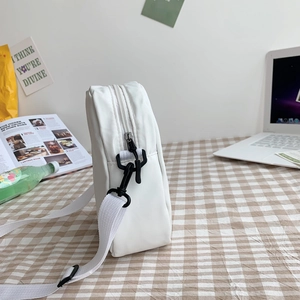 Vue de côté du petit sac bandoulière blanc en nylon avec fermeture éclair sur un bureau