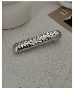 Close-up of silver metal hair tie with textured hammered finish on a beige stone surface