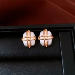 Modern brushed silver oval earrings with golden cross lines on black leather case