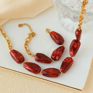 Detailed close-up of gold chain necklace and bracelet set with red marbled natural stones