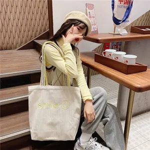 Off-white canvas tote bag with yellow embroidered smile and woven shoulder strap