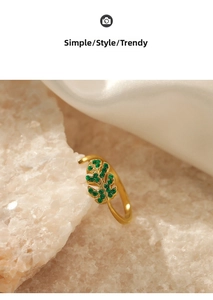 Close-up of leaf-shaped gold ring featuring green crystals on a silk and stone base