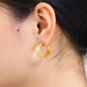 Golden wide C-shape hoop earrings with textured diamond pattern on a model