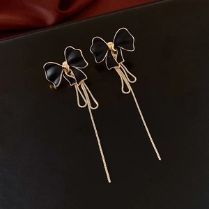 Detail of vintage black bow earrings with long golden tassels on a luxury leather texture