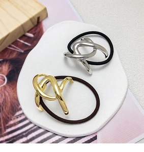 Detail of twisted metal knots in gold and silver on elastic hair ties with textured background