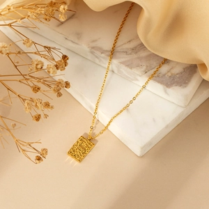 Chic gold lava textured rectangular pendant necklace on white marble with silk accents