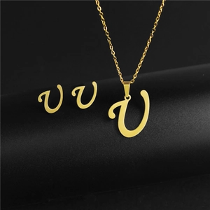 Close-up of golden letter V pendant and matching earrings set on a black pedestal