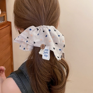 Detail of light gray polka dot scrunchie with button and fabric label on a ponytail