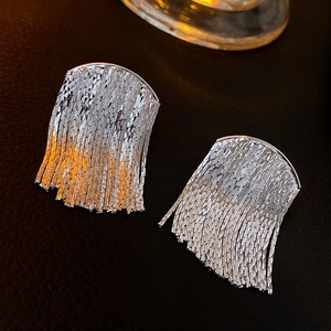 Close-up of silver metal fringe tassel earrings with high-shine finish on leather texture