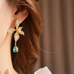 Detail of vintage flower earring with gold petals and a pear-shaped green gemstone