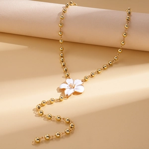 Detail of golden beaded chain with white enamel flower pendant on a beige surface