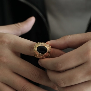 Primer plano de un anillo punk dorado con piedra negra y relieve de cabra.