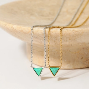 Gold and silver triangle necklaces featuring green opal inlay on a textured stone bowl