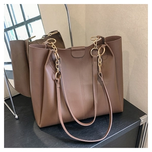 Detail of brown leather tote bag with gold chain strap and vertical stitching accents