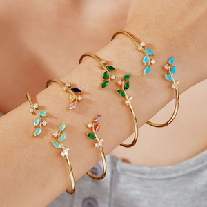 Elegant gold leaf-shaped open cuff bracelet with colorful zircons on a female model's wrist