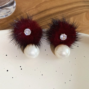 Close-up of red fur ball earrings with pearls and crystals on a rustic textured plate