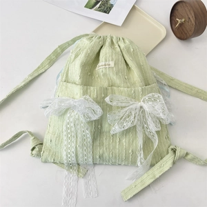 Close-up of mint green canvas backpack with white lace bows and delicate embroidery